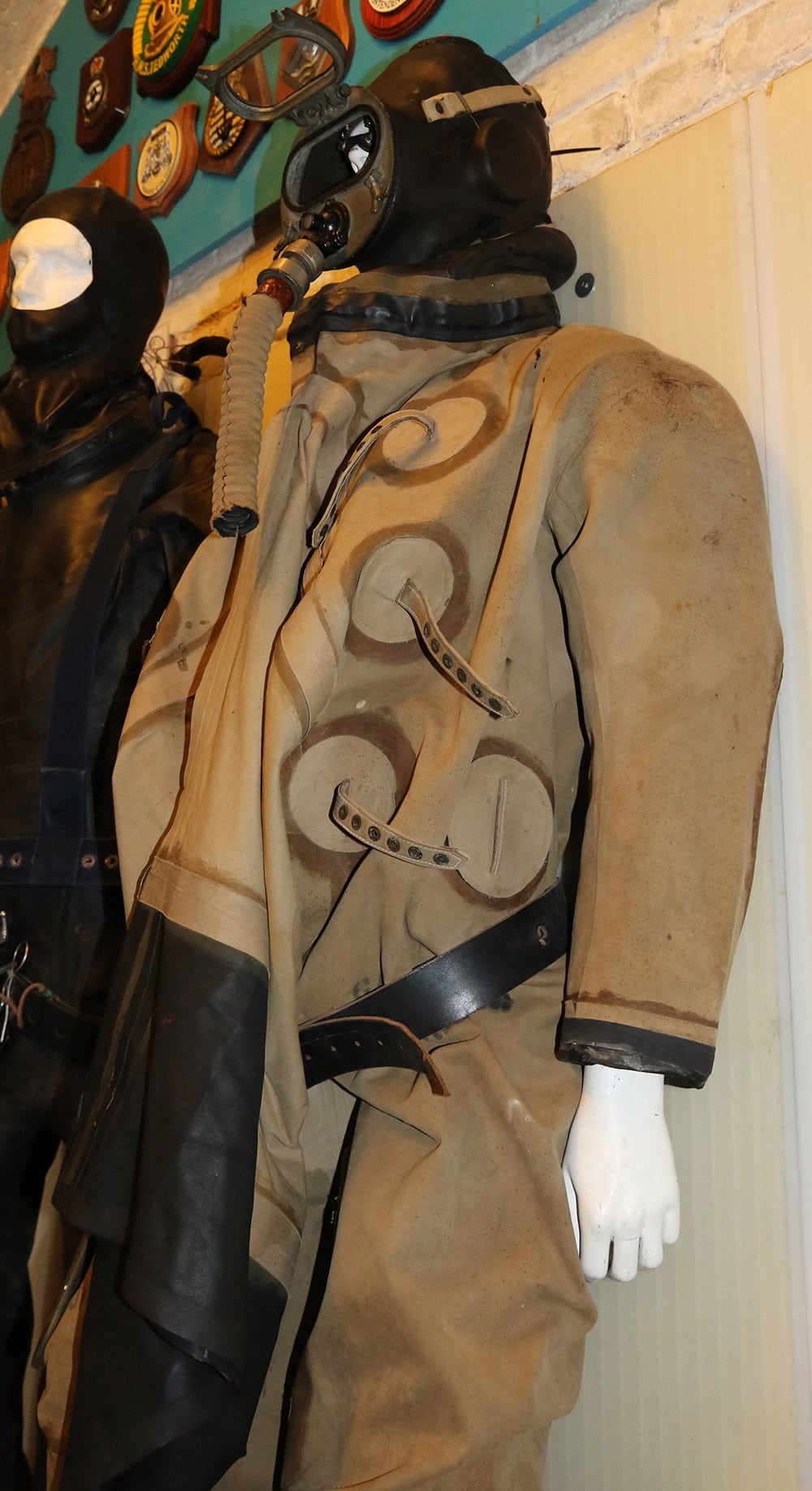 Standing mannequin wearing a canvas suit with built-in rubber hood and mask and large open tunnel-shaped entry sleeve hanging from the waist