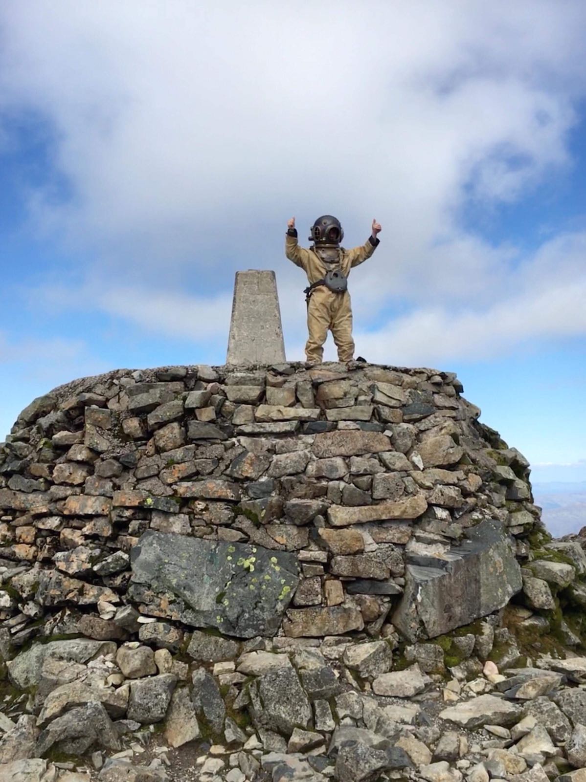A diver in standard diving dress (copper helmet, weights and boots) standing on the summit of Ben Nevis