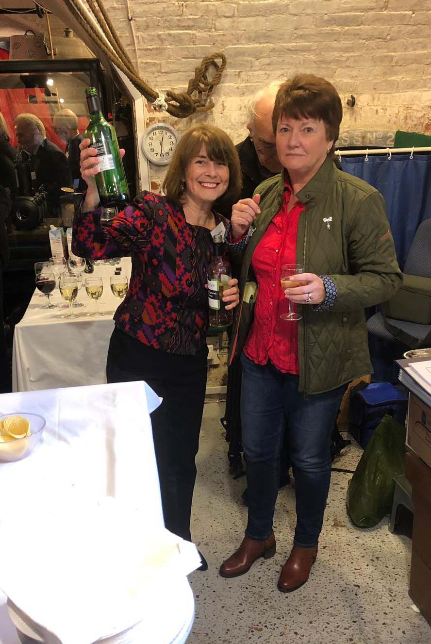 Two volunteers facing the camera. One holding a bottle of wine aloft in celebration.