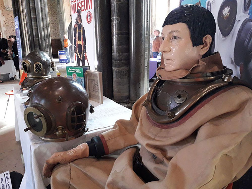 Side view of head and shoulders of man made up to look like a mannequin and dressed in standard diving dress.