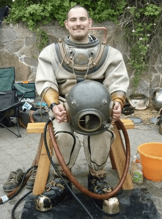 Seated man wearing vintage diver suit holding the helmet on his knees