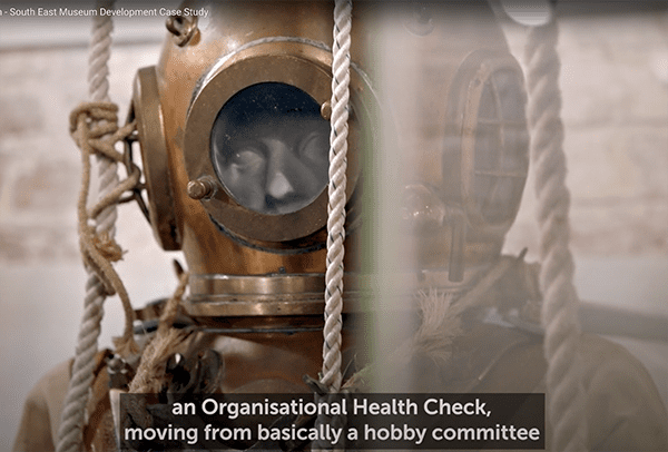 diving helmet in glass case. The helmet appears to be cut in half due to reflections on the glass.