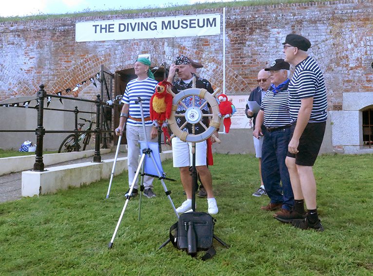 Side view of a barber-shop quartet of singers dressed as pirates on the grass outside the diving museum entrance