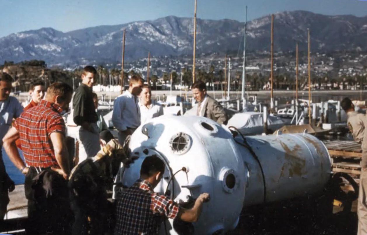 7 or 8 men gathered around the top entry of the observation bell which is lying on its side.
