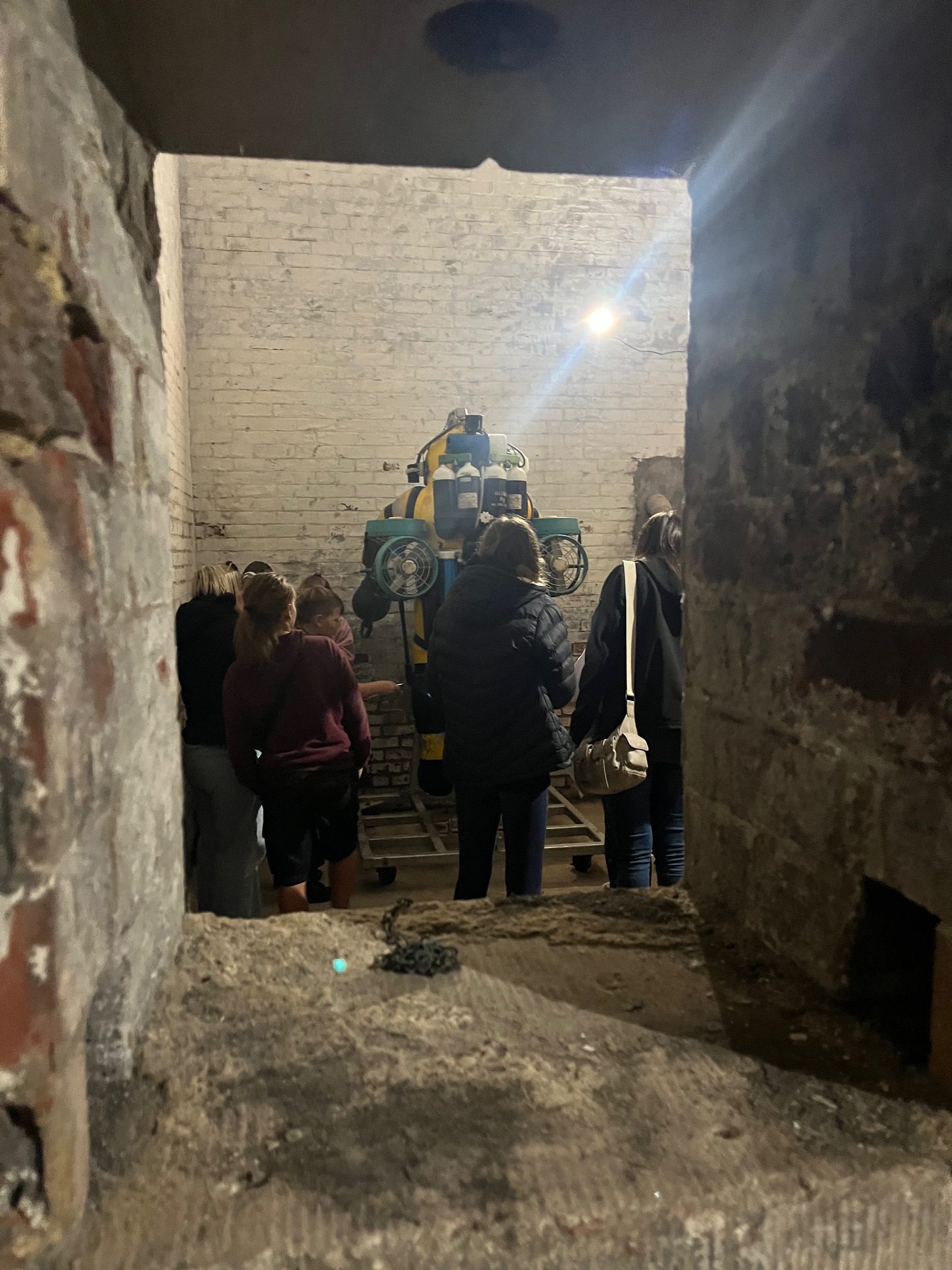 A group of people pictured through a hole in a thick brick wall looking at a deep sea divingsuit